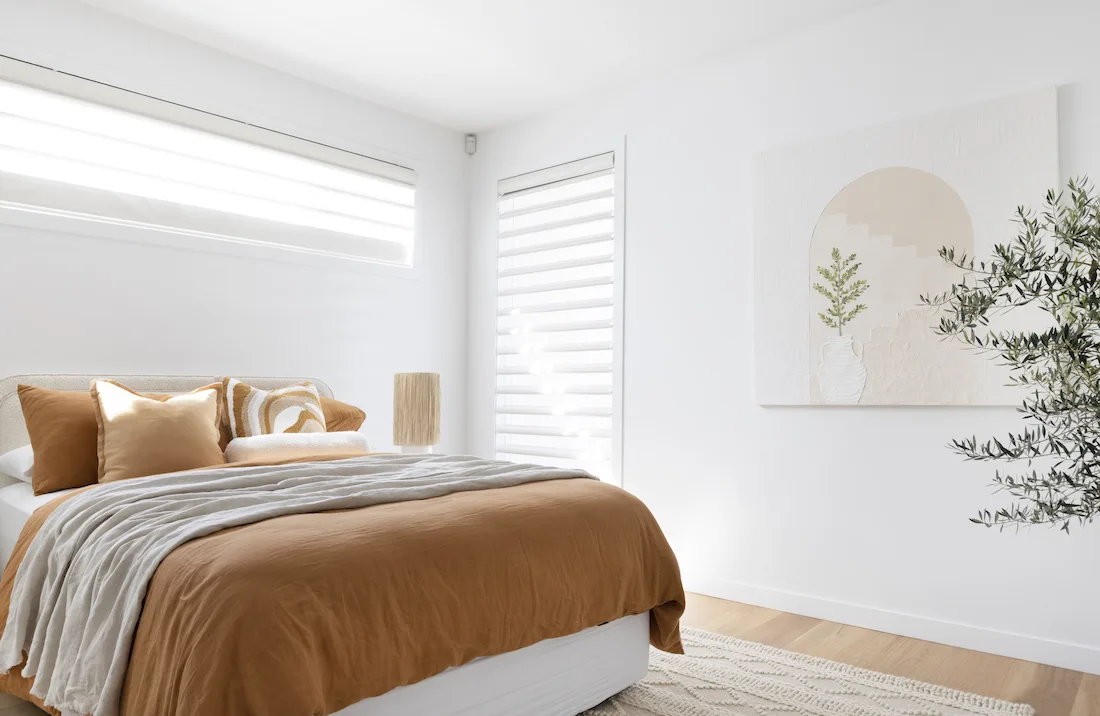 Master bedroom with white walls, artwork and rust coloured bedding