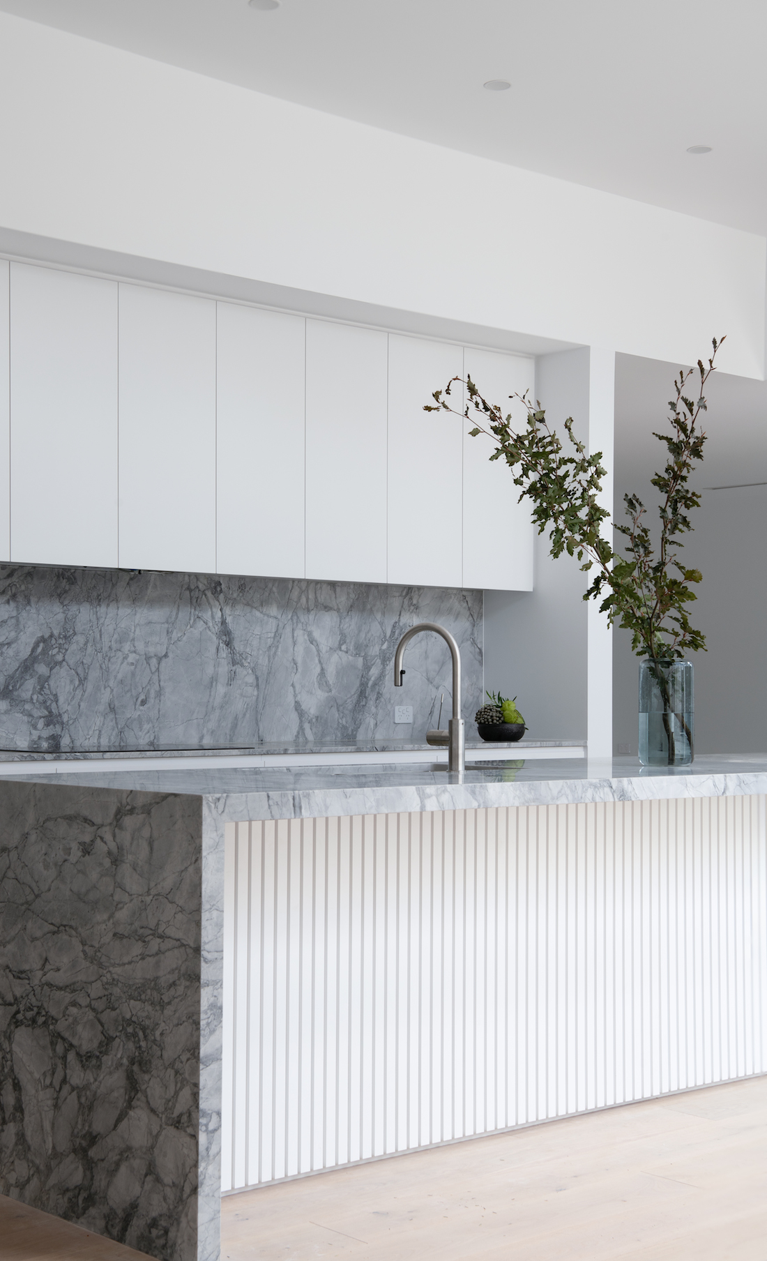 Waterfall stone island bench and white cabinets in kitchen joinery perfection