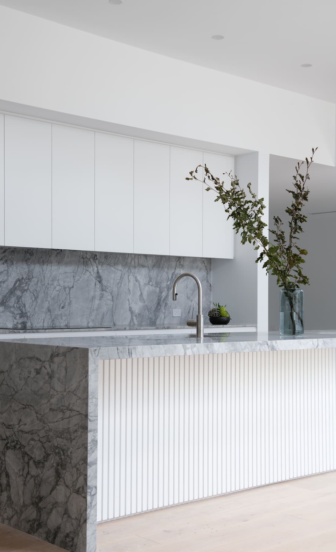 Waterfall stone island bench and white cabinets in kitchen splashbacks