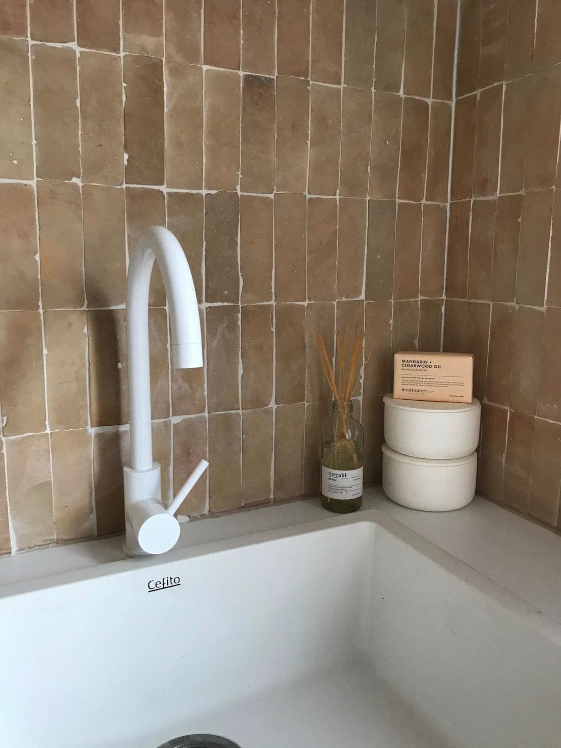 White sink and tap in laundry with pink tiled splashback