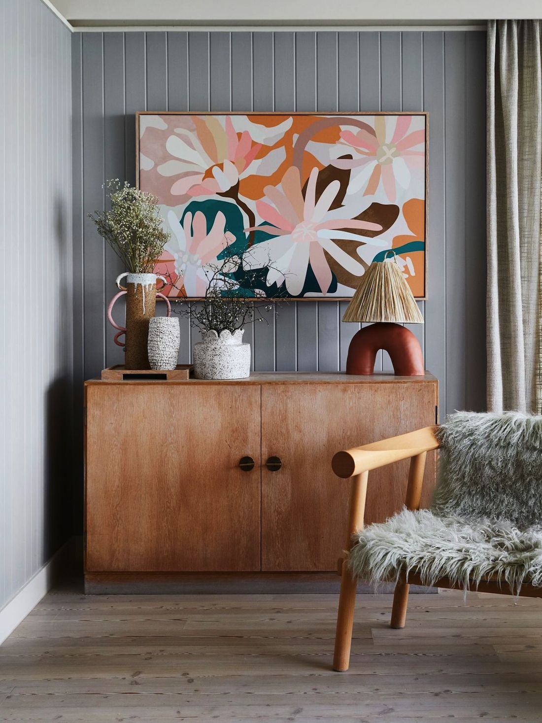 Ceramics atop a sideboard with colourful artwork and fluffy chair