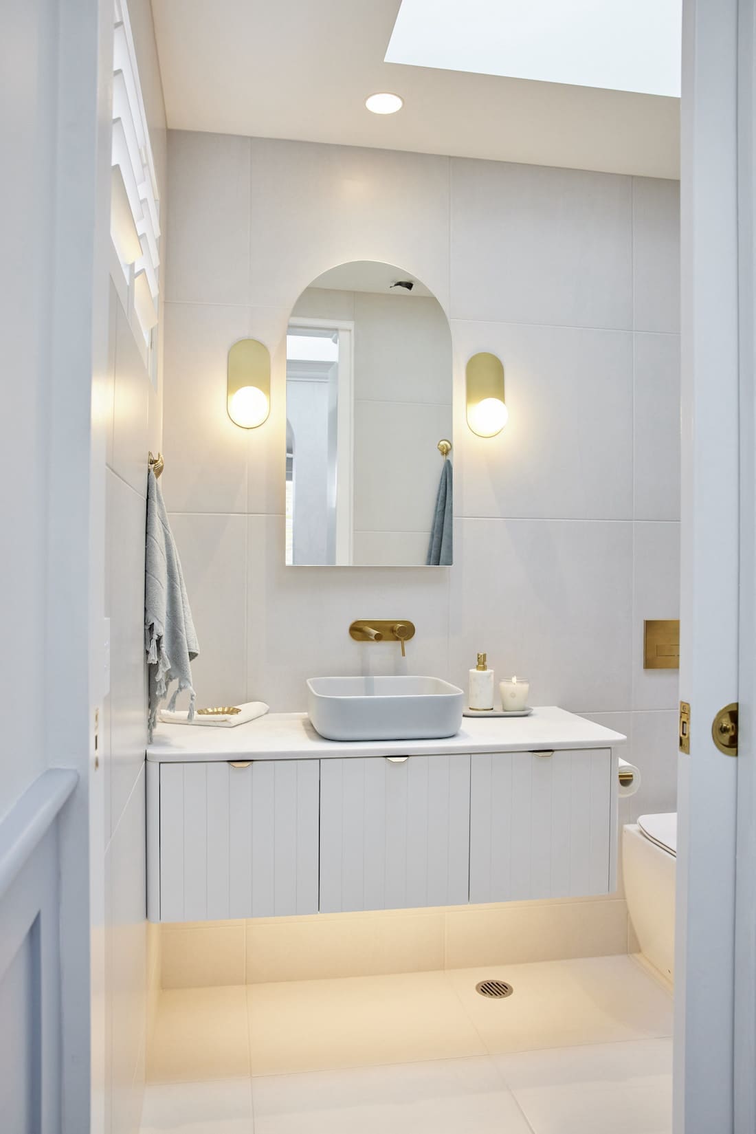 White bathroom with blue sink and arch mirror