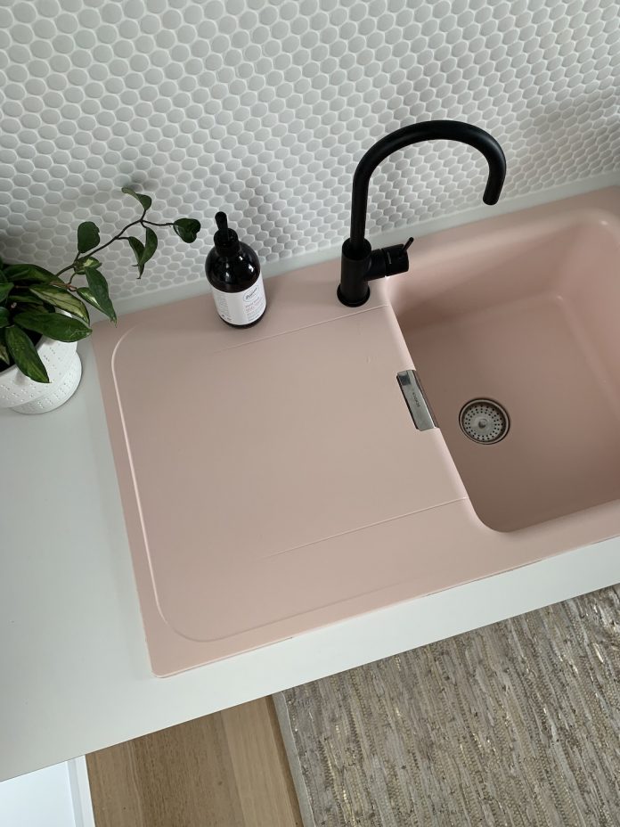 White penny tiles, black tapware, and a pink sink — the chic laundry look