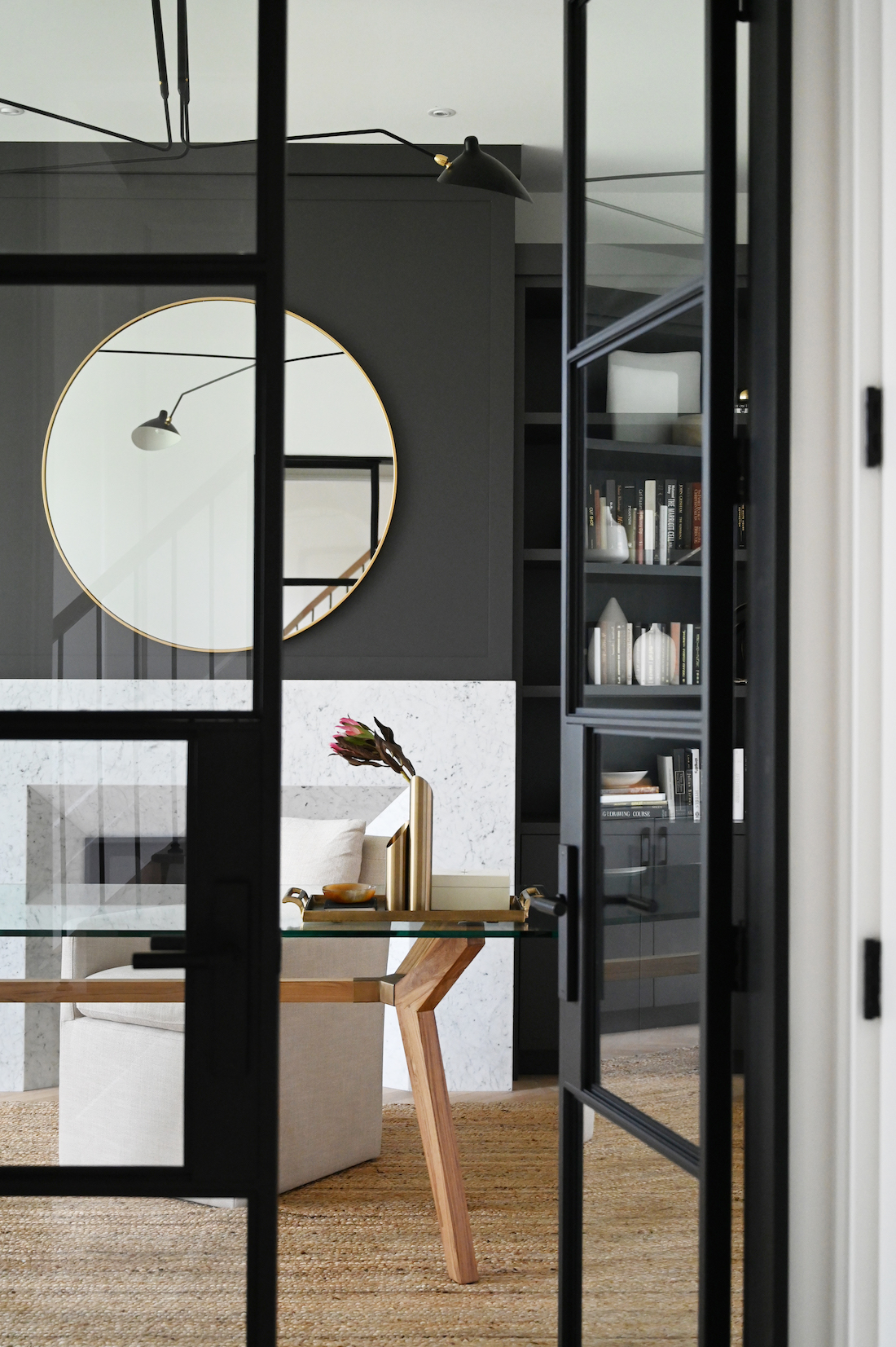 Black framed glass door into study with round mirror