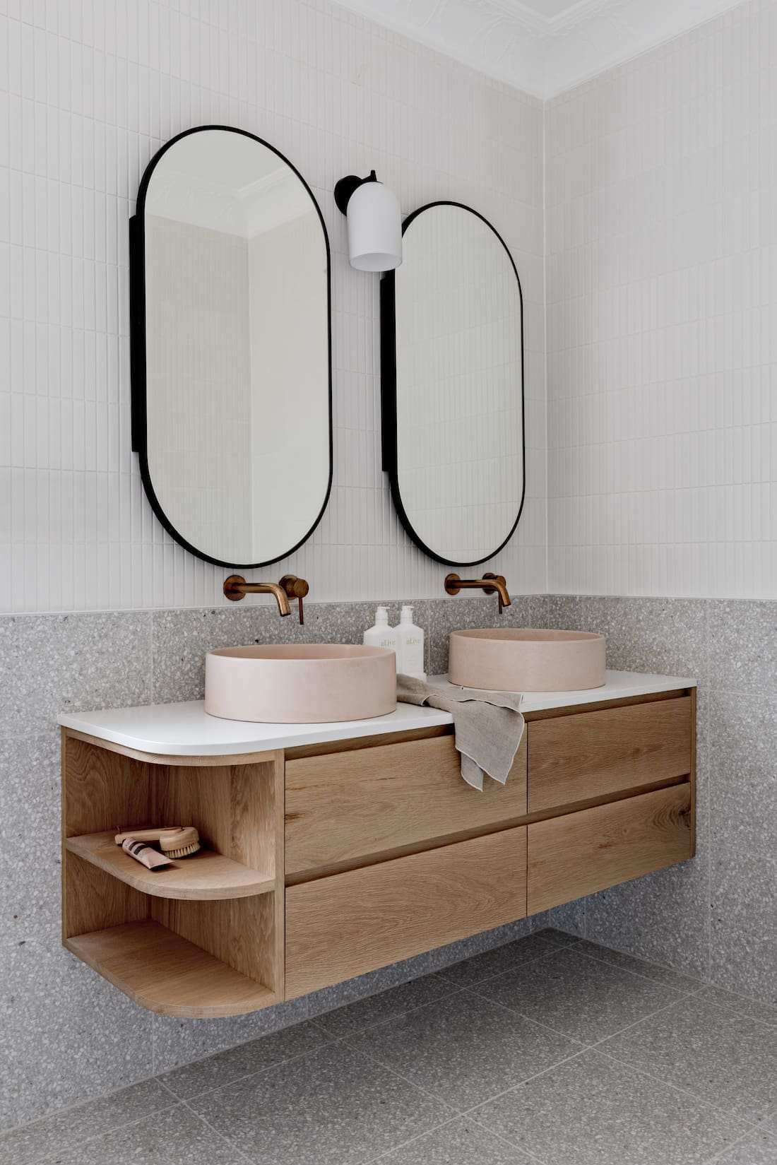 Grey tiles with pink sink and 2 oval mirrors