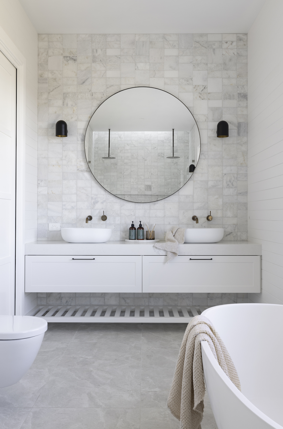 Round mirror in white bathroom with square tiled splashback