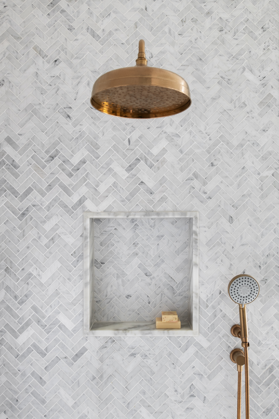 Transcontinental Residence herringbone marble tiles and brass showerhead