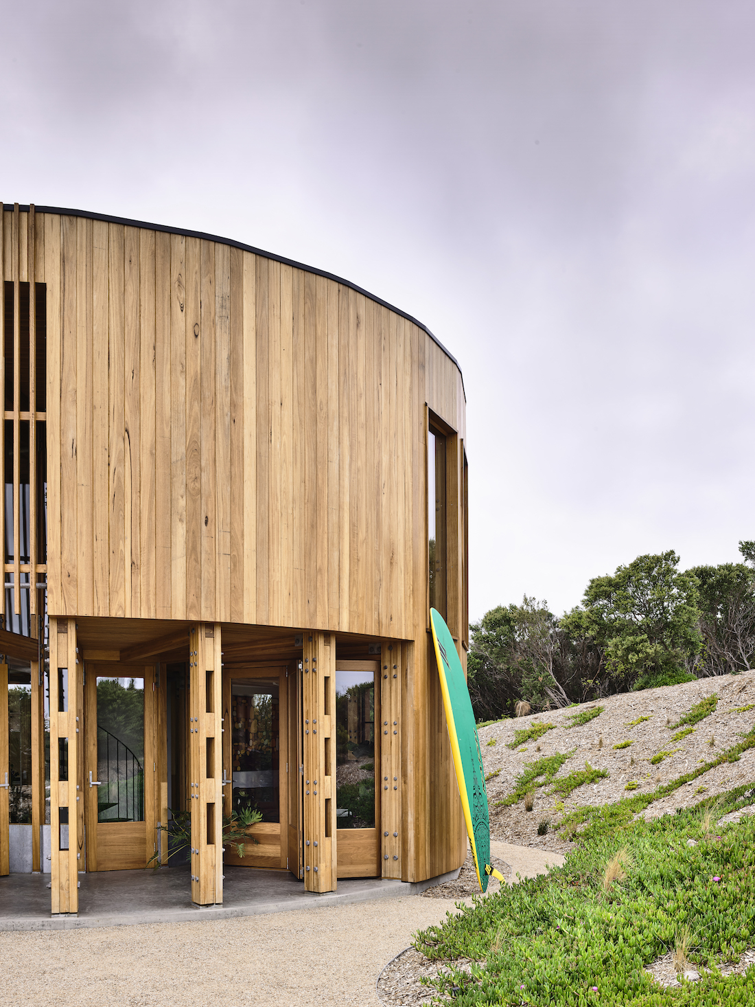 Round timber home in sand dunes with surfboard