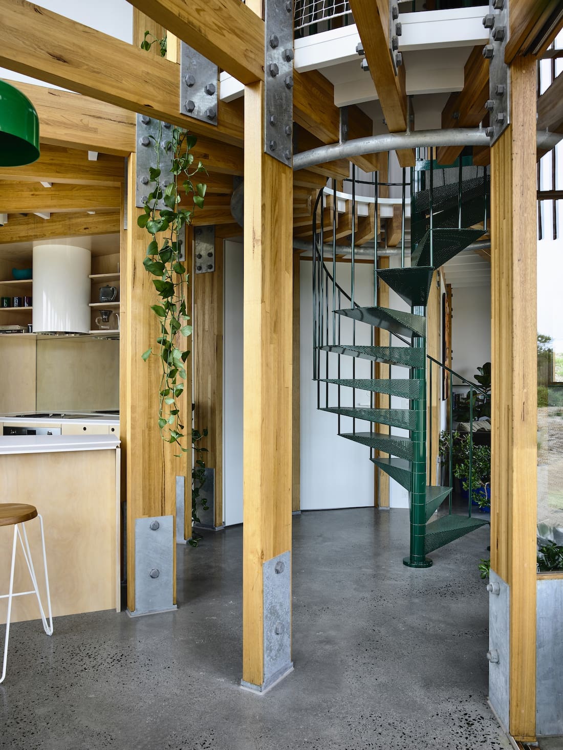 Exposed timber beams and green metal staircase in round house