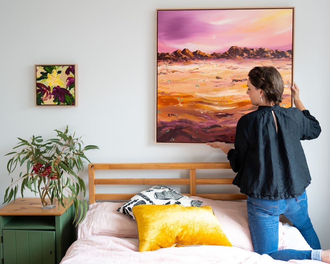 Elle Pervez hanging 2 artworks above bed