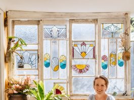 Ivy De Bruijn, the artist behind Ivy's Glass Cottage in front of stained glass art