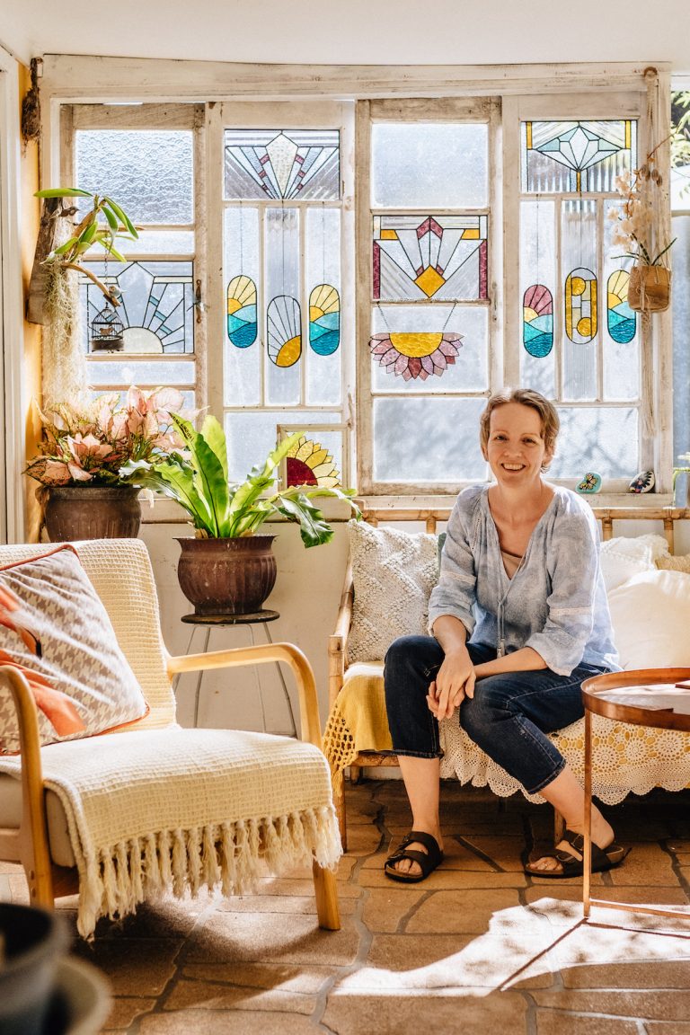 Ivy De Bruijn, the artist behind Ivy's Glass Cottage in front of stained glass art