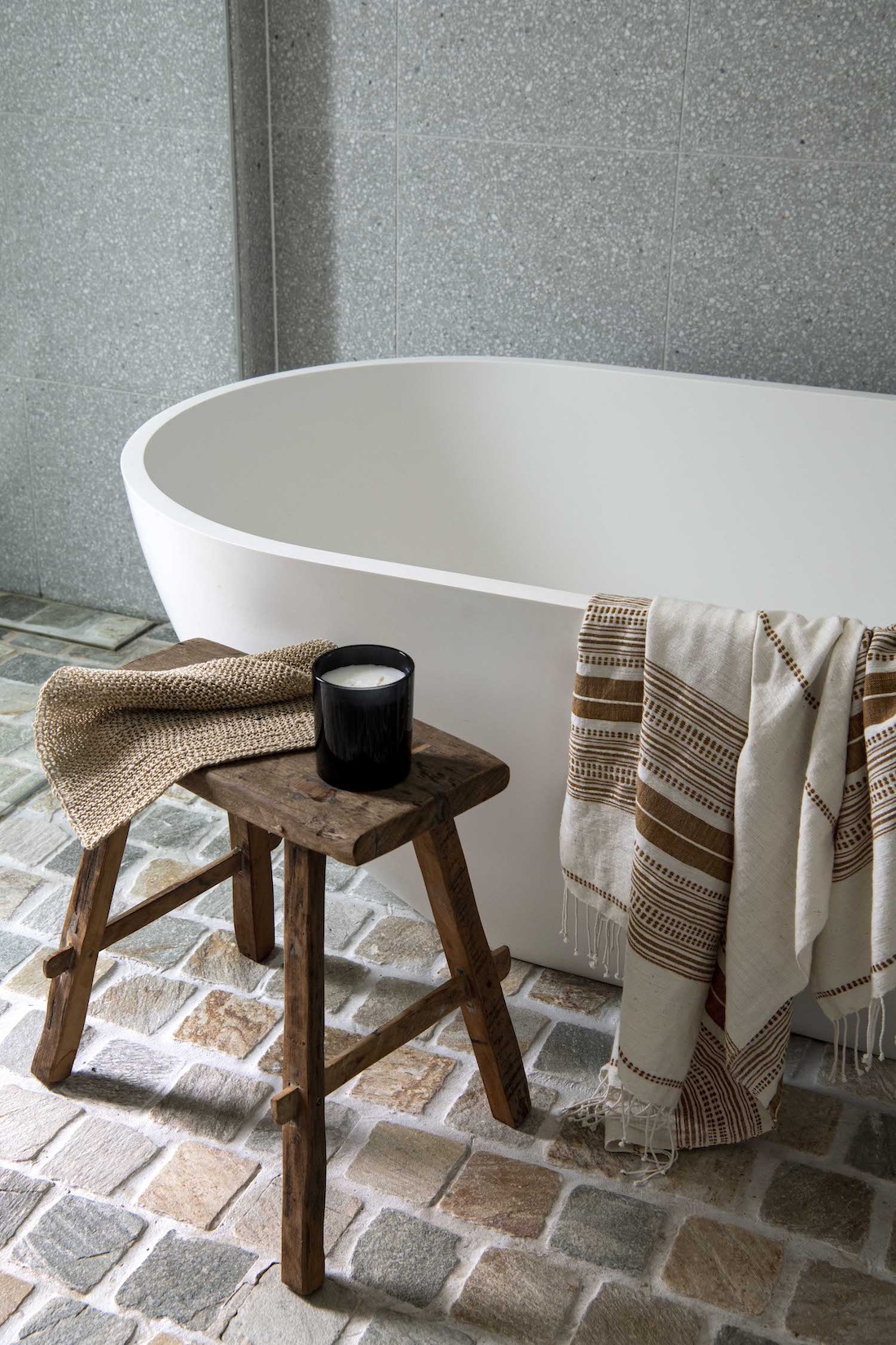 Standalone white bath with cobblestone flooring
