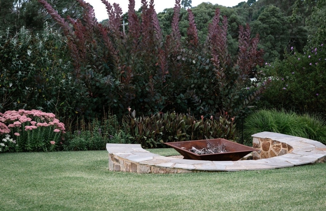 lawn firepit with pink flowers and round stone wall