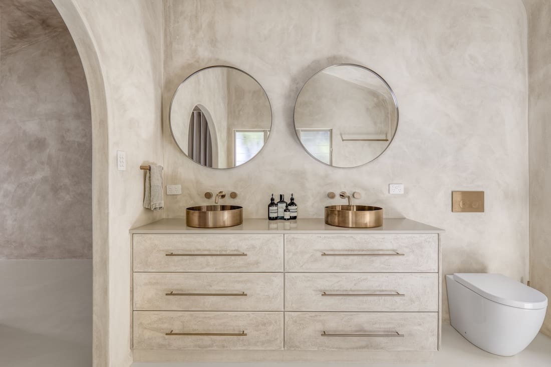Double vanity with round mirrors and copper sinks in bathroom in Ruin X house
