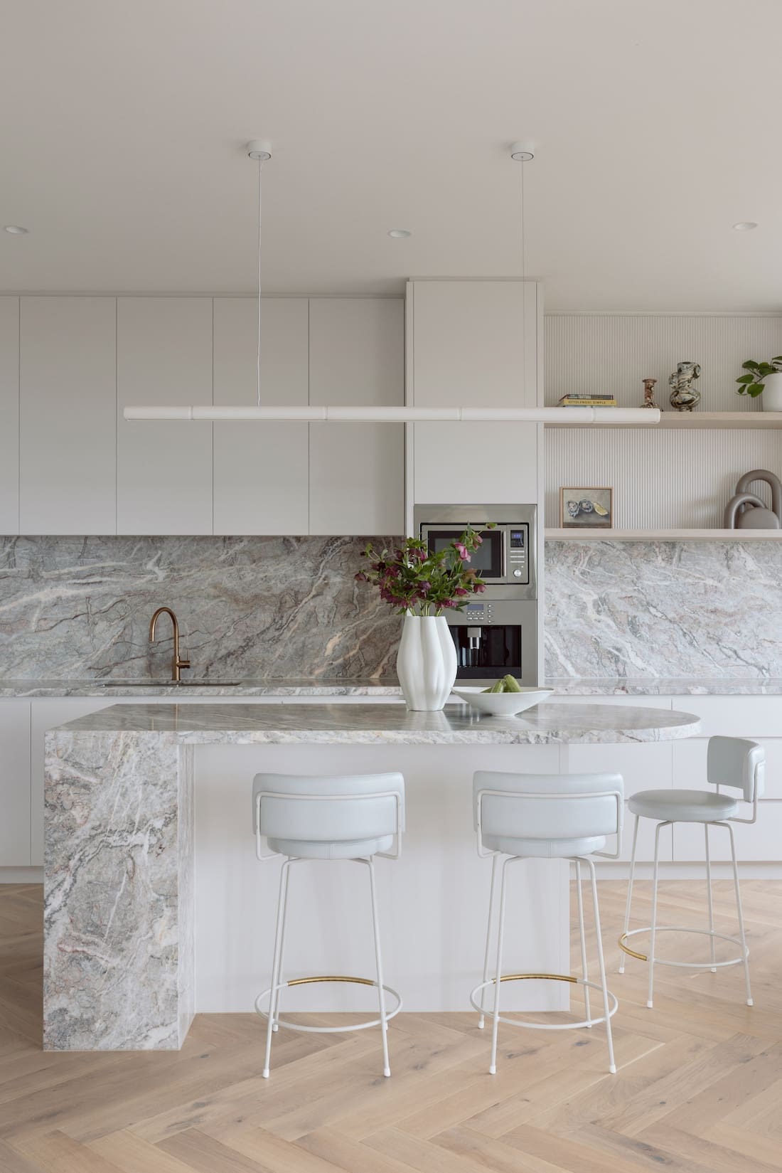 White and marble kitchen with curved island and herringbone flooring