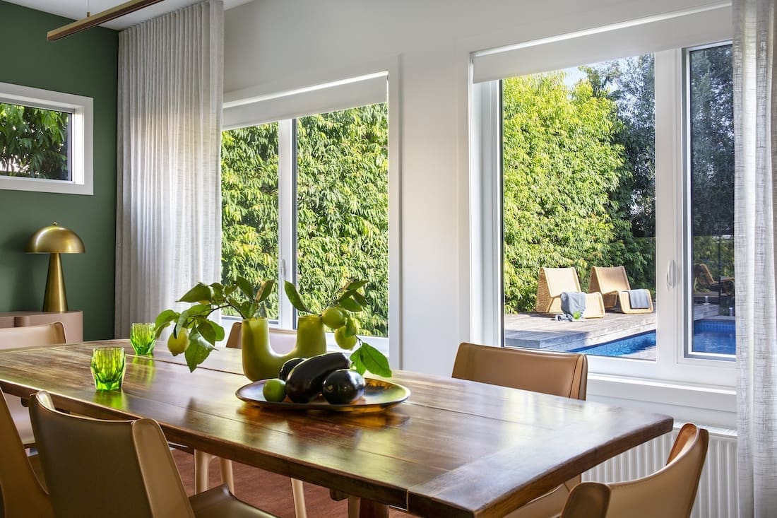 Large windows in dining room looking out on to pool in Warm Embrace residence by The Stylesmiths