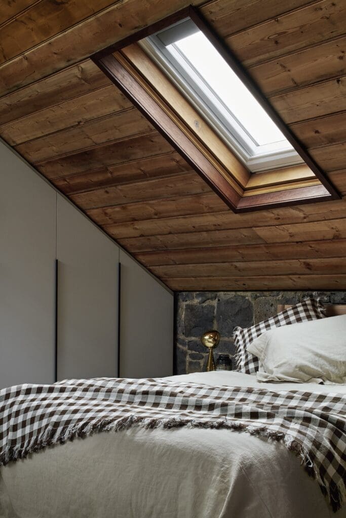 Bedroom with timber-lined sloped ceiling and skylight at Bluestone Sanctuary by The Stylesmiths and YDM Studio, featuring bluestone wall and soft neutral bedding.