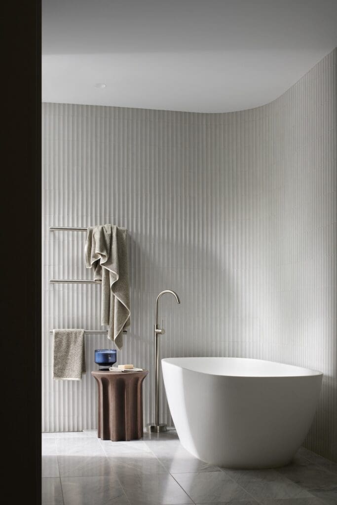Freestanding bathtub in the ensuite at Bluestone Sanctuary with vertically fluted wall tiles, brushed metal floor tap and minimalist bathroom design by The Stylesmiths and YDM Studio.