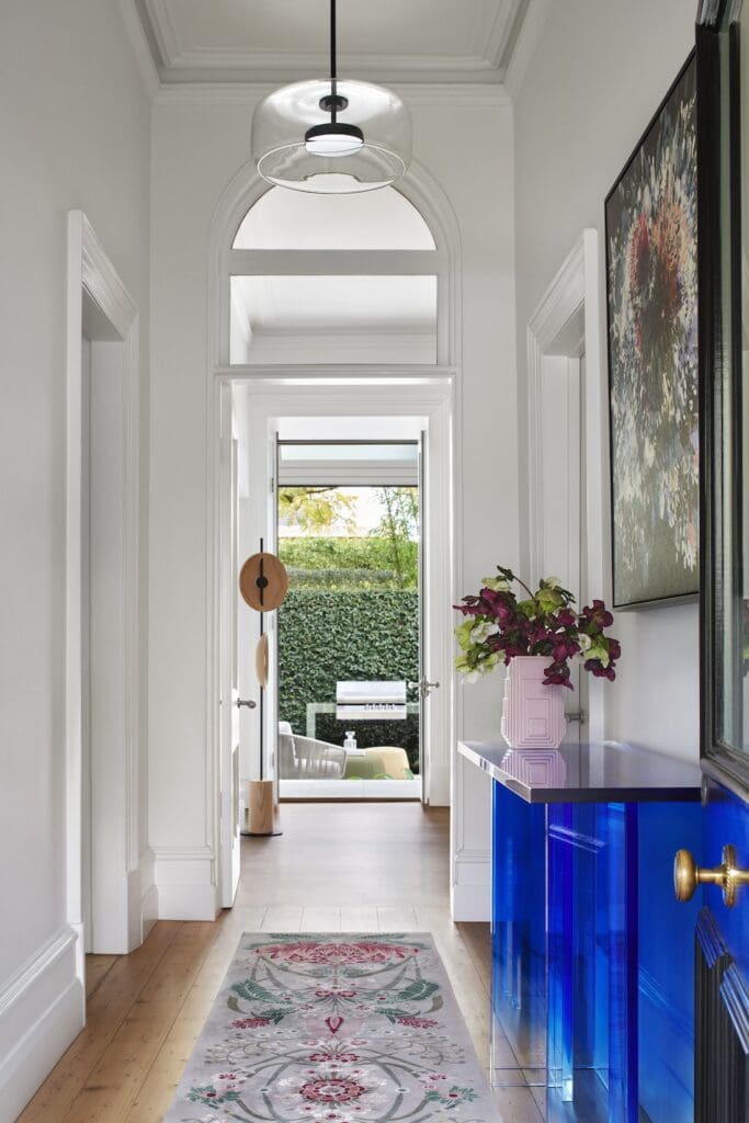 Light-filled hallway at Bluestone Sanctuary with arched doorway, timber floors and contemporary artwork leading to the garden courtyard, designed by The Stylesmiths and YDM Studio.