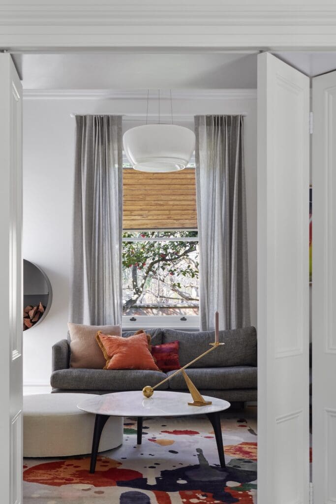 Living room at Bluestone Sanctuary with grey sofa, round coffee table and contemporary artwork rug framed by white double doors, designed by The Stylesmiths and YDM Studio.