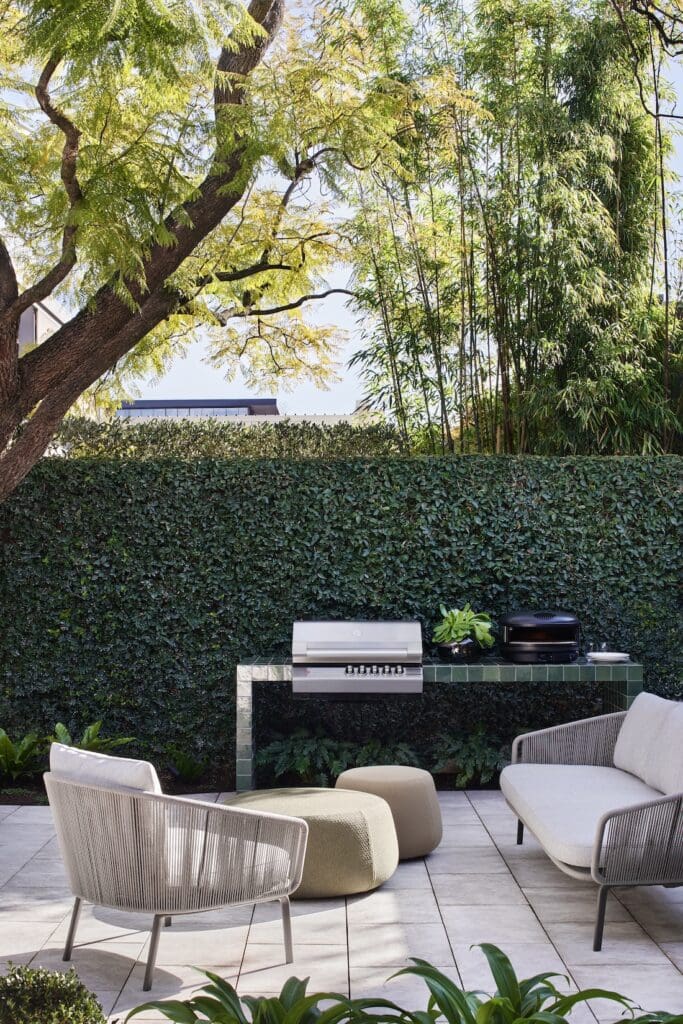Outdoor entertaining area at Bluestone Sanctuary with green tiled BBQ bench, lounge seating and lush garden hedge, designed by The Stylesmiths and YDM Studio.