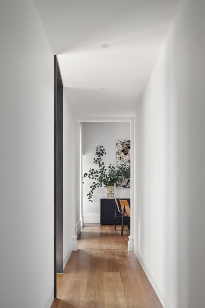 Bright hallway at Bluestone Sanctuary with white walls, timber flooring and view into styled study space, designed by The Stylesmiths with architecture by YDM Studio.