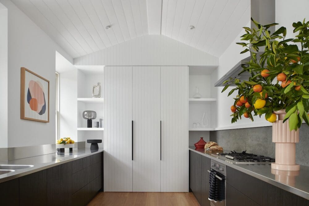 Modern galley kitchen at Bluestone Sanctuary with white V-groove cabinetry, stainless steel benches and citrus arrangement, designed by The Stylesmiths with architecture by YDM Studio.