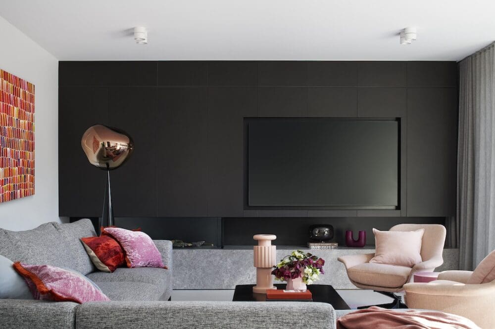 Modern living room at Bluestone Sanctuary with dark feature wall, built-in media unit, grey sofa and soft pink accent chairs, designed by The Stylesmiths and YDM Studio.