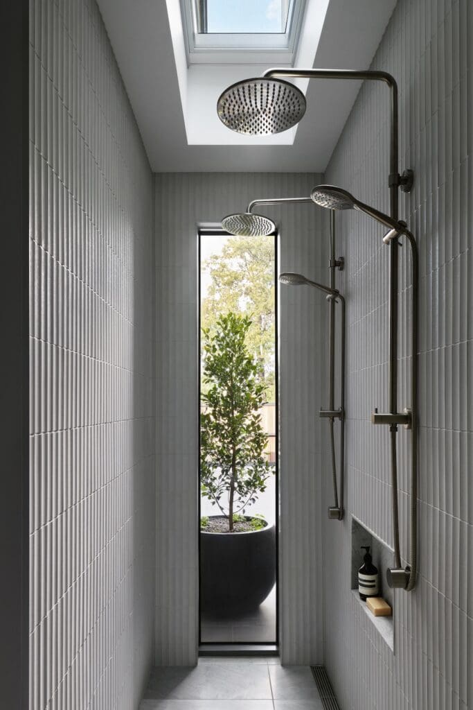 Walk-in shower at Bluestone Sanctuary with vertically fluted tiles, brushed metal shower fittings and skylight above, designed by The Stylesmiths and YDM Studio.