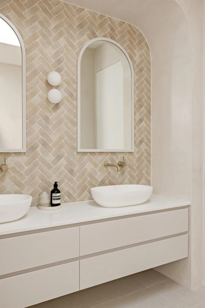 Double vanity with arched mirrors and herringbone tiled bathroom at The Stables Burraneer House
