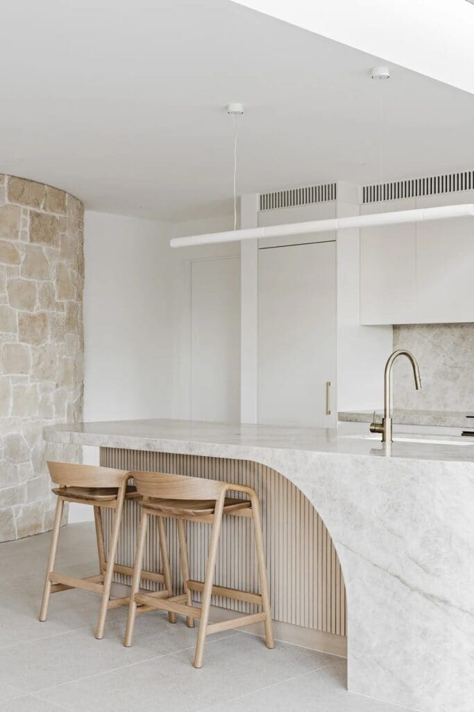 Curved kitchen island bench with natural stone wall at The Stables Burraneer House