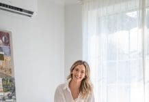 Gina Beschorner sitting in a rust armchair beside a ribbed side table in a light-filled living room.