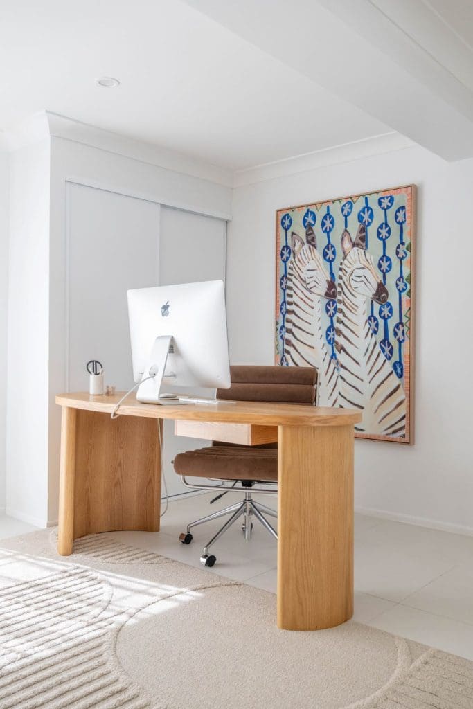 Minimal home office with curved timber desk, brown office chair and large zebra artwork on the wall.