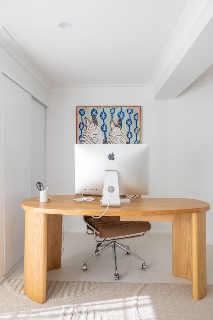 Curved timber desk with iMac computer and brown office chair in a minimalist home office.