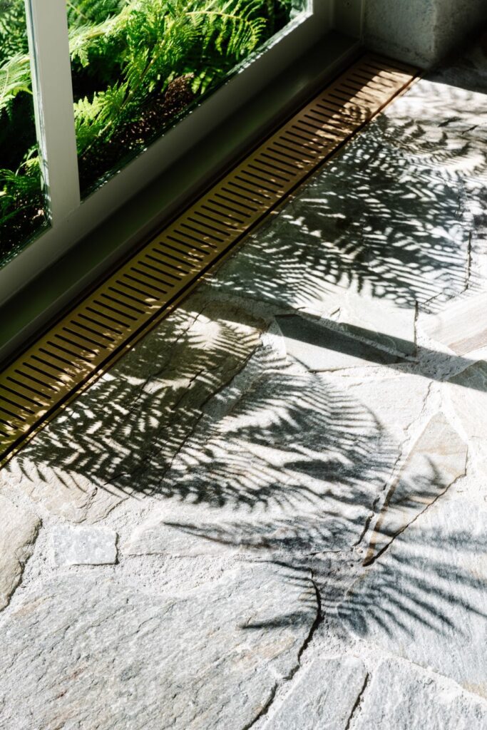 Natural stone flooring with brass linear drain and fern shadows at Mountain House by Breathe, photographed by Marnie Hawson.