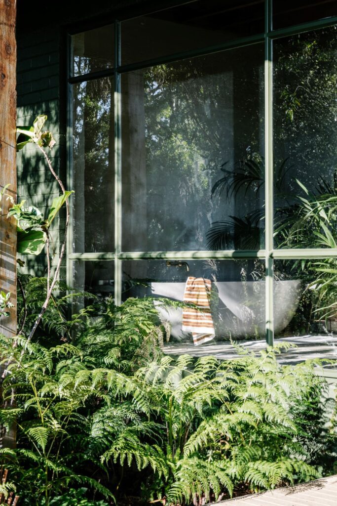Freestanding bathtub behind large glass window surrounded by lush greenery at Mountain House by Breathe, photographed by Marnie Hawson.