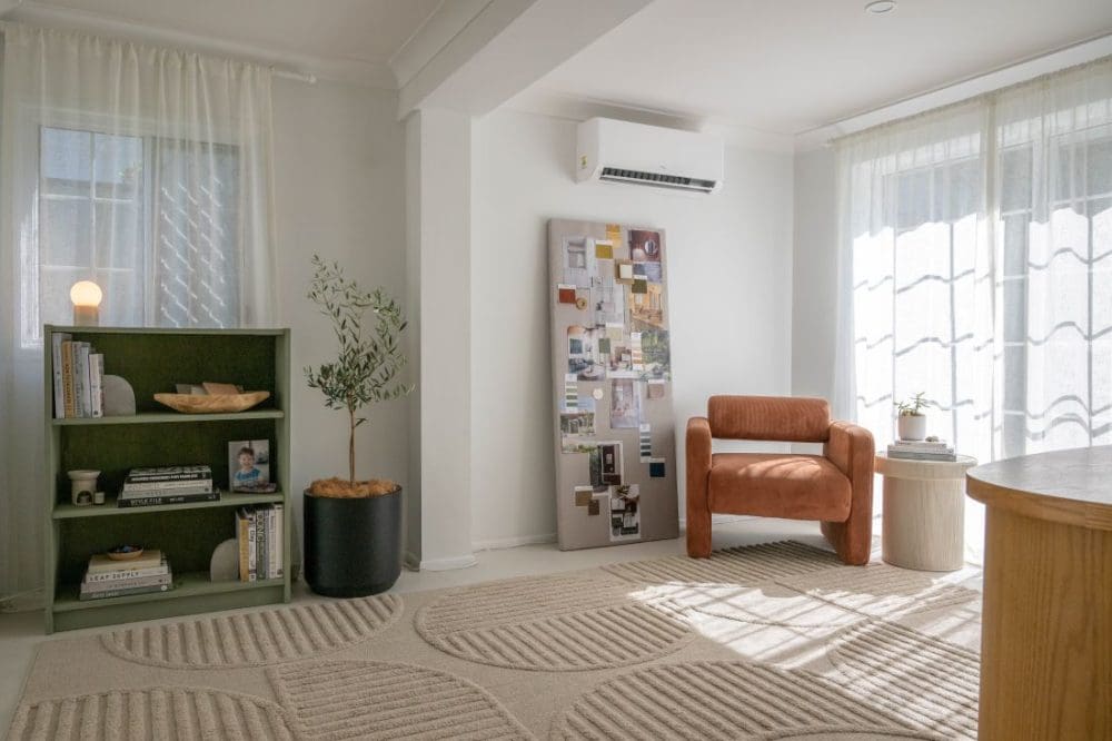 Light-filled living room with olive bookcase, rust armchair, textured rug and sheer curtains.