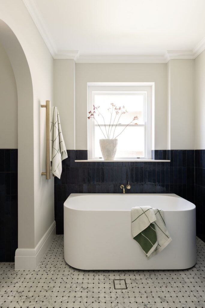 Freestanding bath with navy tiles beneath window