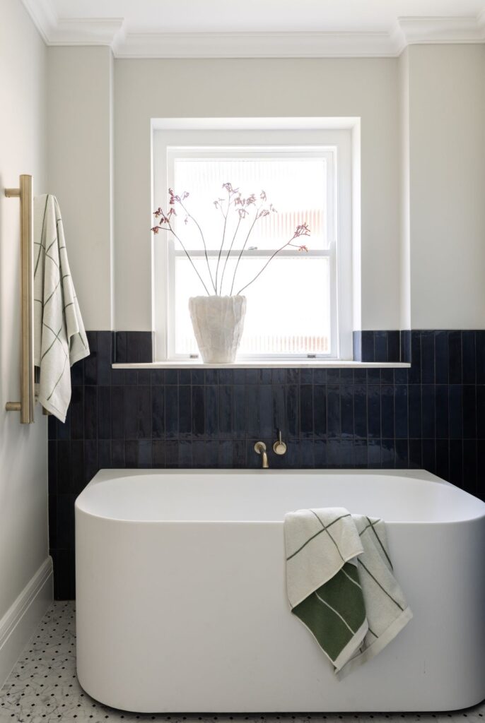 Freestanding bathtub with navy tiled wall and window