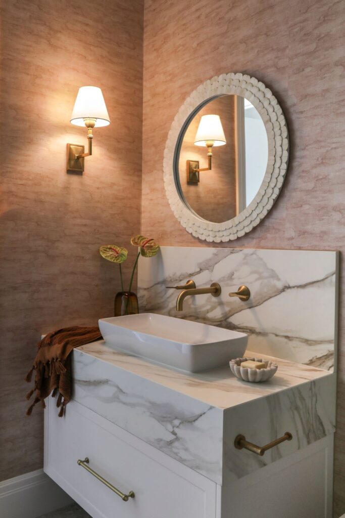 Powder room with marble vanity blush walls and round mirror