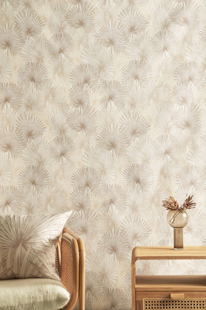 Nobilis_Palm - Sunlit wallpaper featuring a soft beige palm design, complemented by a rattan chair, matching cushion, and a wooden table with a decorative vase.