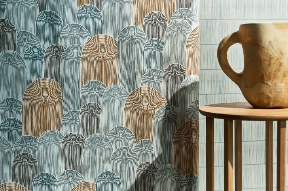 Sanctuary Lines Collection - Haven Textile Fibre wallpaper featuring calming curved patterns in blue and tan hues, paired with a ceramic jug on a wooden table.