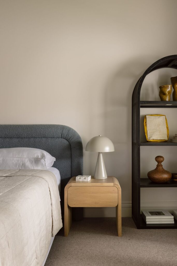 Cosy powder blue upholstered bed head with stylish button table lamp on a curved timber side table