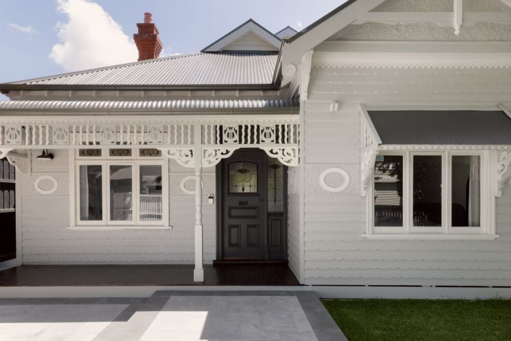 A charming traditional home exterior featuring intricate woodwork, a dark front door, and large windows, with a beautifully paved entryway