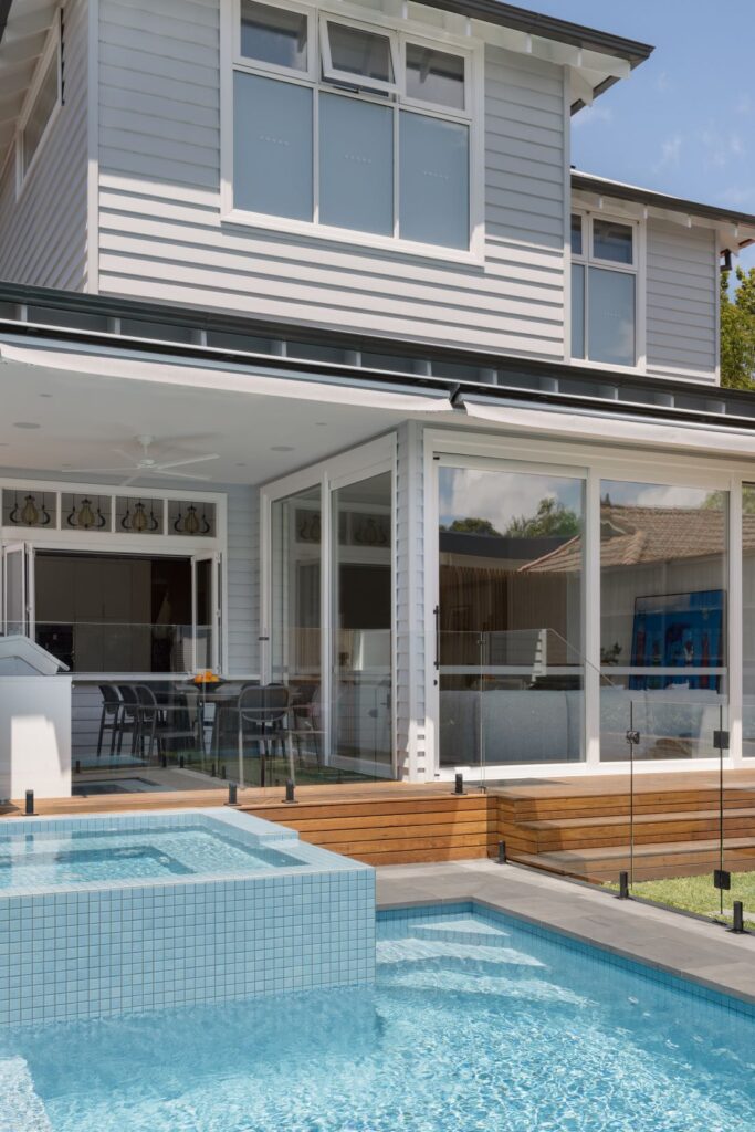 A modern outdoor area featuring a pool with a spa, wooden decking, and a glass railing