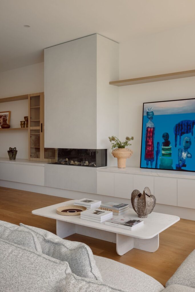 A sleek modern living room featuring a built-in fireplace, white cabinetry, and a vibrant piece of artwork above the mantel