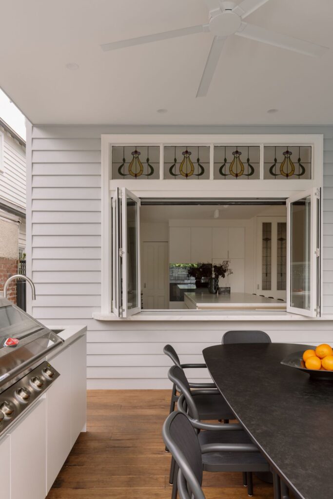 A modern kitchen with an open window that connects to an outdoor dining space with a round table and chairs
