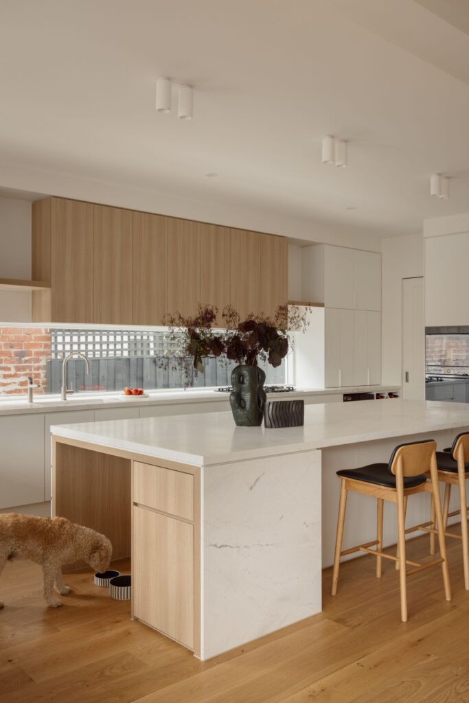 A spacious kitchen featuring a sleek marble countertop island, wooden cabinetry, and contemporary light fixtures