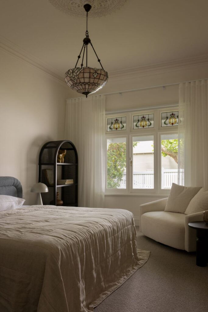 A tranquil bedroom featuring a large bed, modern light fixture, a comfortable armchair, and decorative stained-glass windows